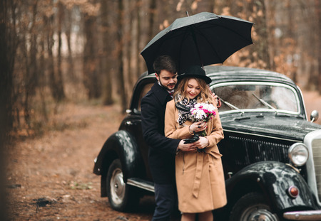 Romantic fairytale wedding couple, bride and groom, kissing and embracing in pine forest near retro car.の写真素材