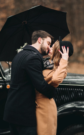 Romantic fairytale wedding couple, bride and groom, kissing and embracing in pine forest near retro car.の写真素材