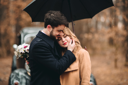 Romantic fairytale wedding couple, bride and groom, kissing and embracing in pine forest near retro car.の写真素材