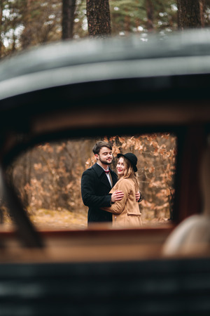 Romantic fairytale wedding couple, bride and groom, kissing and embracing in pine forest near retro car.の写真素材
