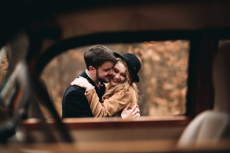 Romantic fairytale wedding couple, bride and groom, kissing and embracing in pine forest near retro car.の写真素材
