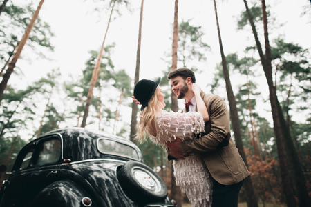 Romantic fairytale wedding couple, bride and groom, kissing and embracing in pine forest near retro car.の写真素材