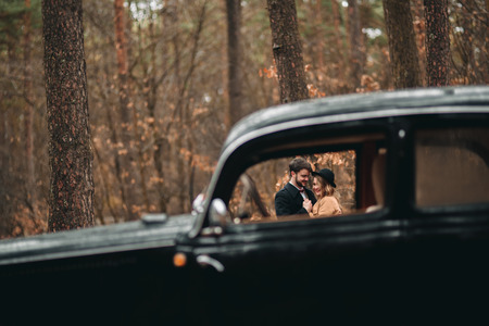 Romantic fairytale wedding couple, bride and groom, kissing and embracing in pine forest near retro car.の写真素材