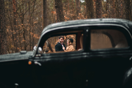 Romantic fairytale wedding couple, bride and groom, kissing and embracing in pine forest near retro car.の写真素材