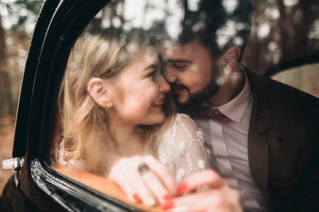 Romantic fairytale wedding couple, bride and groom, kissing and embracing in pine forest near retro car.の写真素材