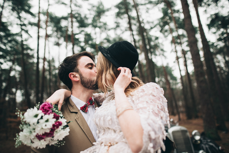 Romantic fairytale wedding couple, bride and groom, kissing and embracing in pine forest near retro car.の写真素材
