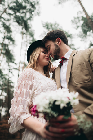 Romantic fairytale wedding couple, bride and groom, kissing and embracing in pine forest near retro car.の写真素材