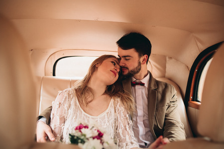 Romantic fairytale wedding couple, bride and groom, kissing and embracing in pine forest near retro car.の写真素材