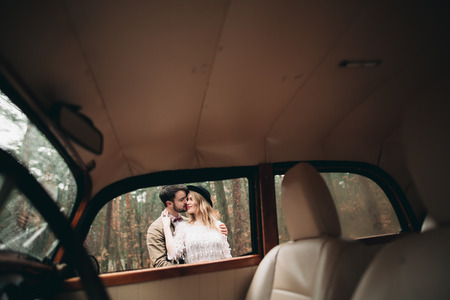 Romantic fairytale wedding couple, bride and groom, kissing and embracing in pine forest near retro car.の写真素材