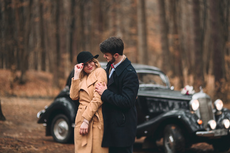 Romantic fairytale wedding couple, bride and groom, kissing and embracing in pine forest near retro car.の写真素材