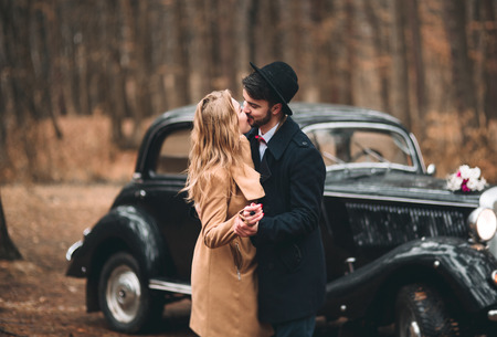 Romantic fairytale wedding couple, bride and groom, kissing and embracing in pine forest near retro car.の写真素材