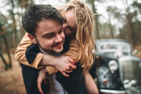 Romantic fairytale wedding couple, bride and groom, kissing and embracing in pine forest near retro car.の写真素材