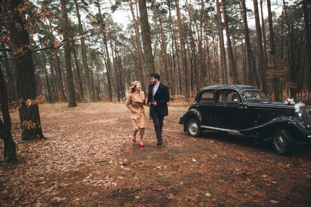 Romantic fairytale wedding couple, bride and groom, kissing and embracing in pine forest near retro car.の写真素材