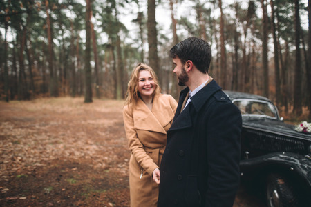 Romantic fairytale wedding couple, bride and groom, kissing and embracing in pine forest near retro car.の写真素材