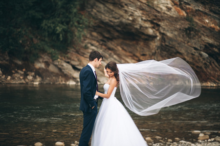 Elegant gentle stylish groom and bride near river with stones.の写真素材