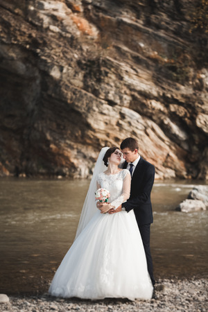Handsome romantic groom and beautiful bride posing near river in scenic mountains.の写真素材
