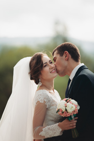 Handsome romantic groom and beautiful bride posing near river in scenic mountains.の写真素材