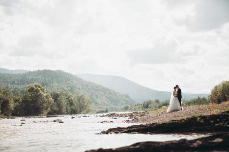 Beautiful wedding couple stay on stone of the river in scenic mountains.の写真素材