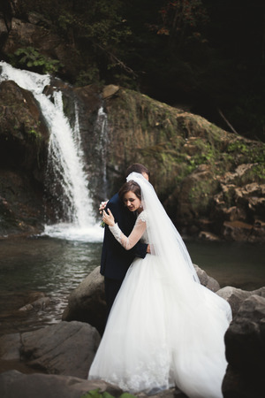 Beautiful wedding couple stay on stone of the river in scenic mountains.の写真素材