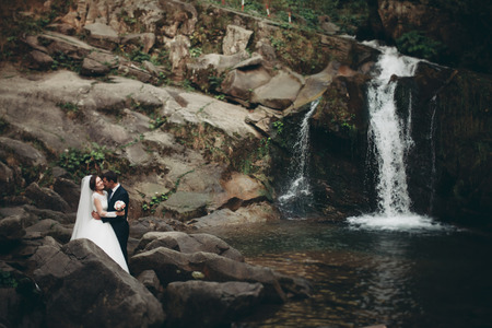 Beautiful wedding couple stay on stone of the river in scenic mountains.の写真素材