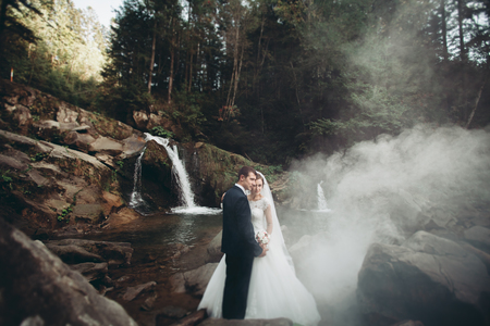 Beautiful wedding couple stay on stone of the river in scenic mountains.の写真素材