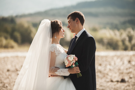Handsome romantic groom and beautiful bride posing near river in scenic mountains.の写真素材