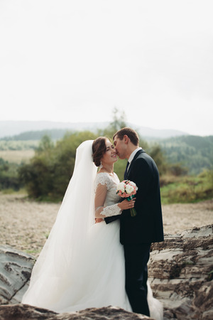 Handsome romantic groom and beautiful bride posing near river in scenic mountains.の写真素材