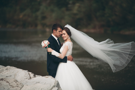 Handsome romantic groom and beautiful bride posing near river in scenic mountains.の写真素材