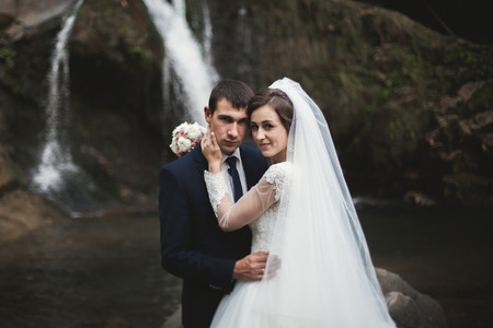Beautiful wedding couple stay on stone of the river in scenic mountains.の写真素材
