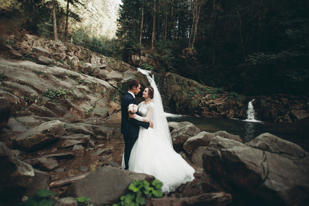Beautiful wedding couple stay on stone of the river in scenic mountains.の写真素材