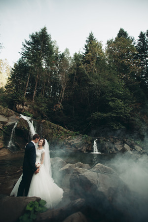 Beautiful wedding couple stay on stone of the river in scenic mountains.の写真素材