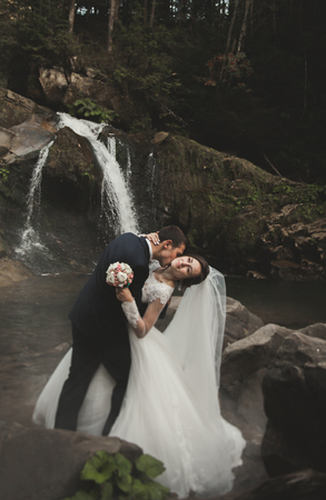 Beautiful wedding couple stay on stone of the river in scenic mountains.の写真素材