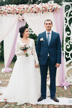 Wedding couple standing under an arch of fresh flowers.の写真素材