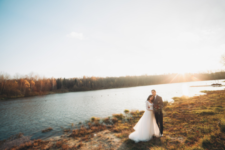 Elegant beautiful wedding couple posing near a lake at sunset.の写真素材