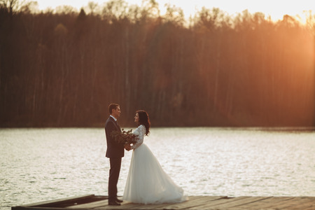 Elegant beautiful wedding couple posing near a lake at sunset.の写真素材