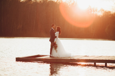 Elegant beautiful wedding couple posing near a lake at sunset.の写真素材