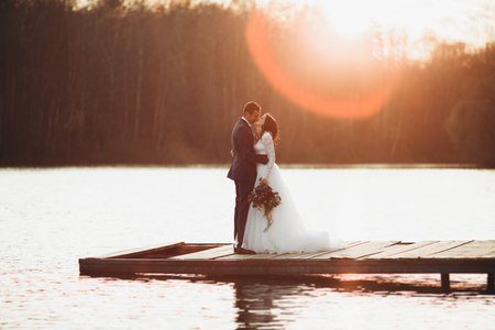 Elegant beautiful wedding couple posing near a lake at sunset.の写真素材