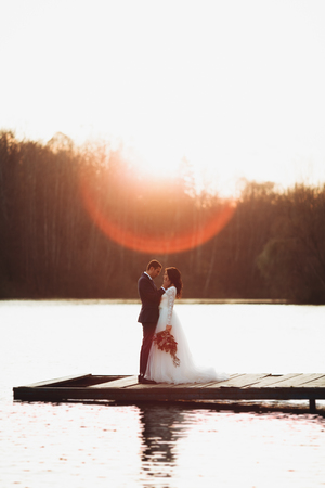 Elegant beautiful wedding couple posing near a lake at sunset.の写真素材