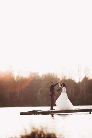 Elegant beautiful wedding couple posing near a lake at sunset.の写真素材