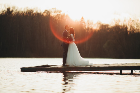Elegant beautiful wedding couple posing near a lake at sunset.の写真素材