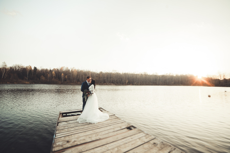 Elegant beautiful wedding couple posing near a lake at sunset.の写真素材
