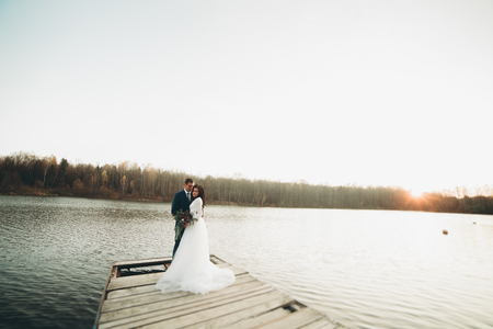 Elegant beautiful wedding couple posing near a lake at sunset.の写真素材