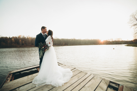 Elegant beautiful wedding couple posing near a lake at sunset.の写真素材