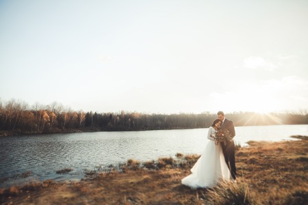 Elegant beautiful wedding couple posing near a lake at sunset.の写真素材