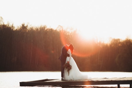 Elegant beautiful wedding couple posing near a lake at sunset.の写真素材