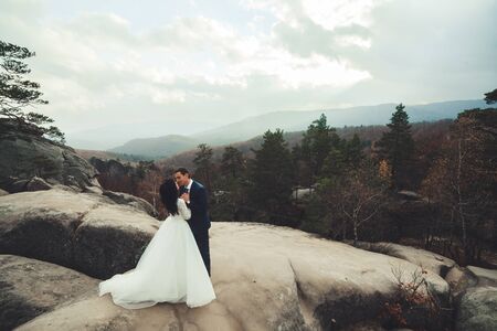 Gorgeous bride and groom kissing and hugging near the cliffs with stunning views.の写真素材