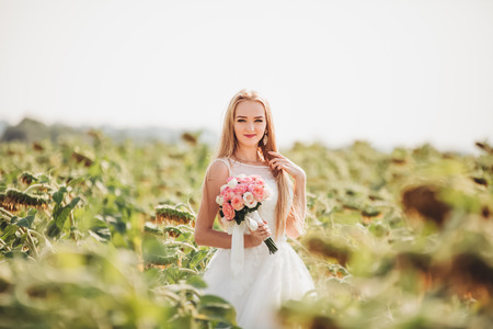 Elegant blonde bride with long hair and a bouquet of sunflowers in the field.の写真素材