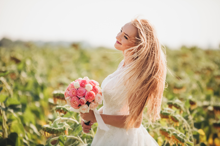 Elegant blonde bride with long hair and a bouquet of sunflowers in the field.の写真素材