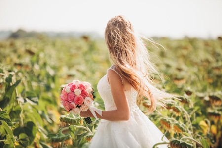Elegant blonde bride with long hair and a bouquet of sunflowers in the field.の写真素材