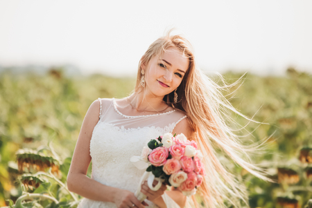 Elegant blonde bride with long hair and a bouquet of sunflowers in the field.の写真素材